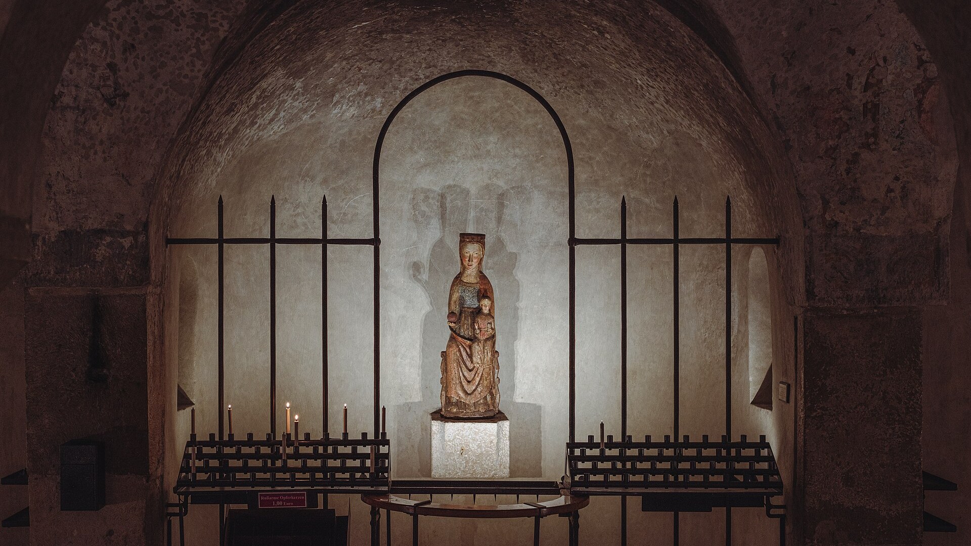 Vigil candles burning before a statue of Mary in a stone shrine niche